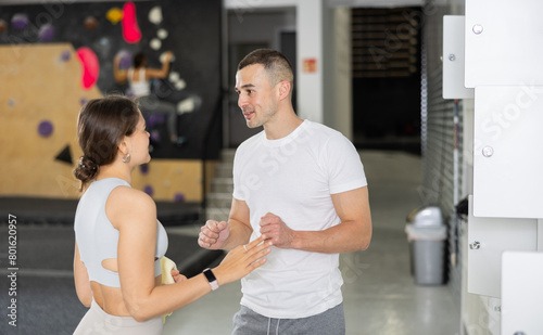 In locker room of gym  female and male clients engaged in conversation. These young people standing and exchanged few words after changing into workout attire and getting ready for exercise session.