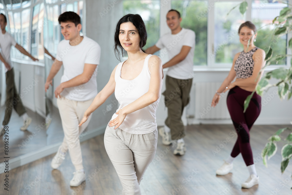 Obraz premium Sporty smiling young brunette practicing rhythmic aerobics during group workout in fitness studio. Active lifestyle concept
