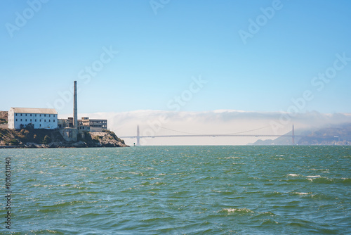 View of Alcatraz Island in San Francisco Bay, CA, USA. The Federal prison buildings and the Golden Gate Bridge are visible in the backdrop, creating a contrast between nature and history.
