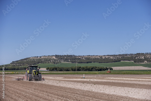 A green tractor pulling a red plow through a crop field with a forested mountain behind © Toyakisfoto.photos