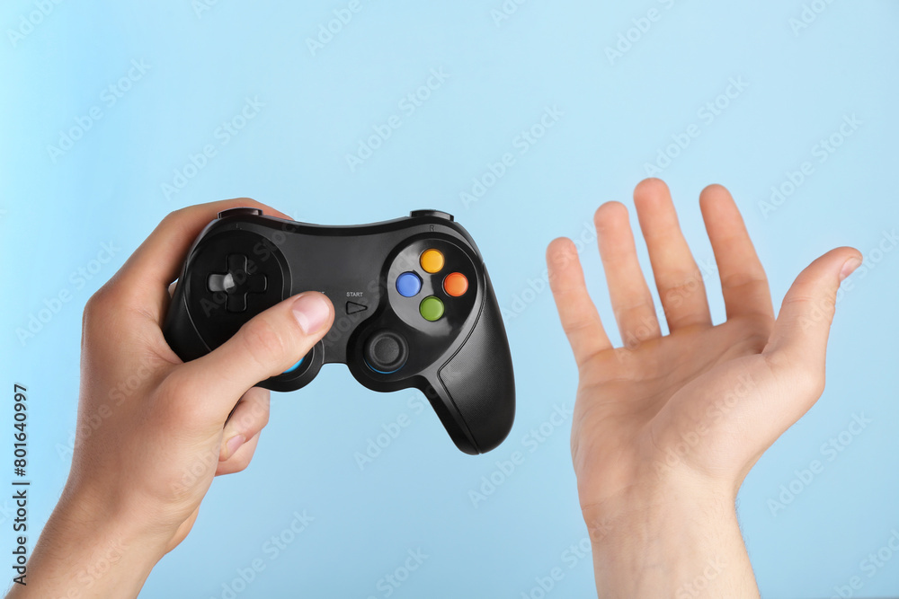 Fototapeta premium Man using wireless game controller on light blue background, closeup