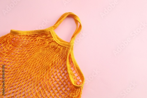 Orange string bag on pink background, top view. Space for text