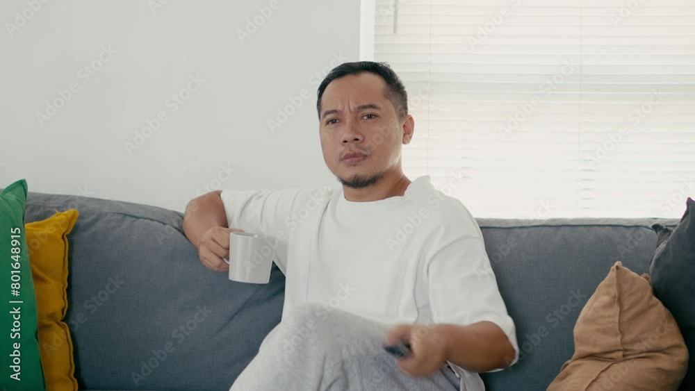 Asian Man Sitting on Sofa Enjoying Drinks and Switching Remote Control and Surprised and Stress Looking at Bad News on Tv Asian Man Sitting on Sofa Enjoying Drinks and Switching Remote Control and Surprised and Stress Looking at Bad News on Tv