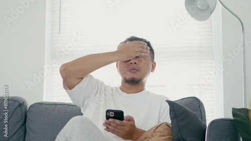 Asian Man Checking Smartphone and Getting Bad News, Feel Sad and Frustated at Home  photo