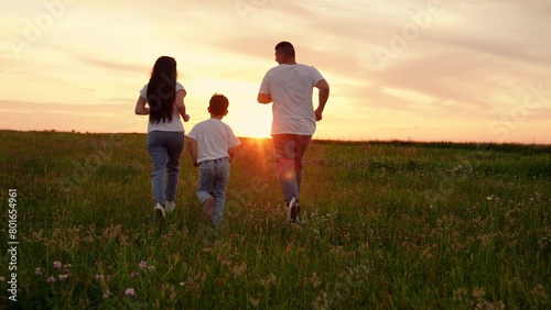 Dad baby mom play together in meadow. Family runs across meadow together toward sunset. Joyful parents enjoy getaway with young son in open air. Mother, father with child enjoy active life in nature.