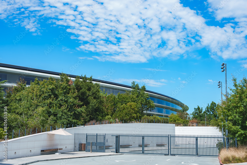 Modern, sleek curved building in Mountain View, California. Surrounded by greenery with blue sky. Gated entrance with white fence, no people or products shown.