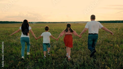 Happy children with father and mother playing on green meadow at sunset. Happy family, Children with parents run across field. Children parents playfully enjoy time spent together on weekend on park
