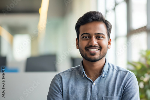 Cheerful young man with a friendly smile wearing a casual denim shirt posing in a bright, contemporary office setting, exuding confidence and approachability