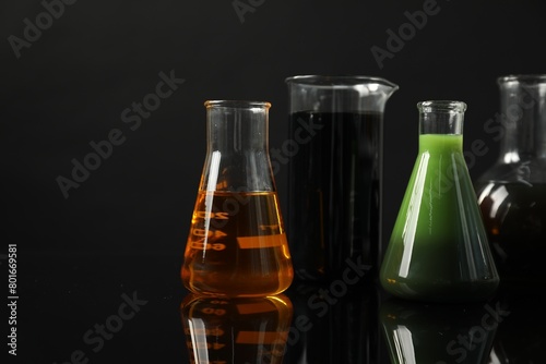 Glass flasks and beaker with different types of oil on black background photo