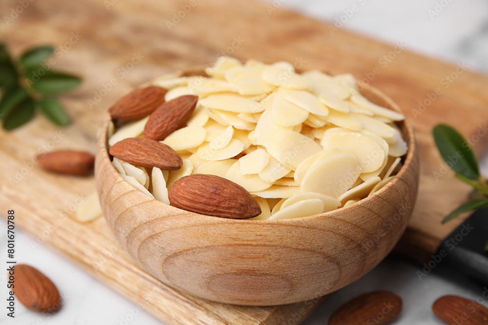 Fresh almond flakes and nuts in bowl on white table, closeup