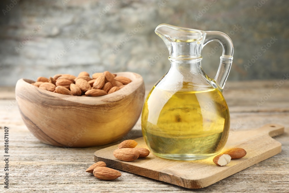 Almond oil in jug and nuts on wooden table, closeup Almond oil in jug and nuts on wooden table, closeup