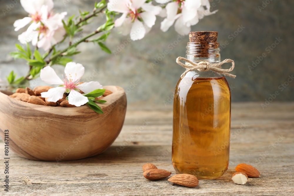 Almond oil in bottle, flowers and nuts on wooden table, closeup Almond oil in bottle, flowers and nuts on wooden table, closeup
