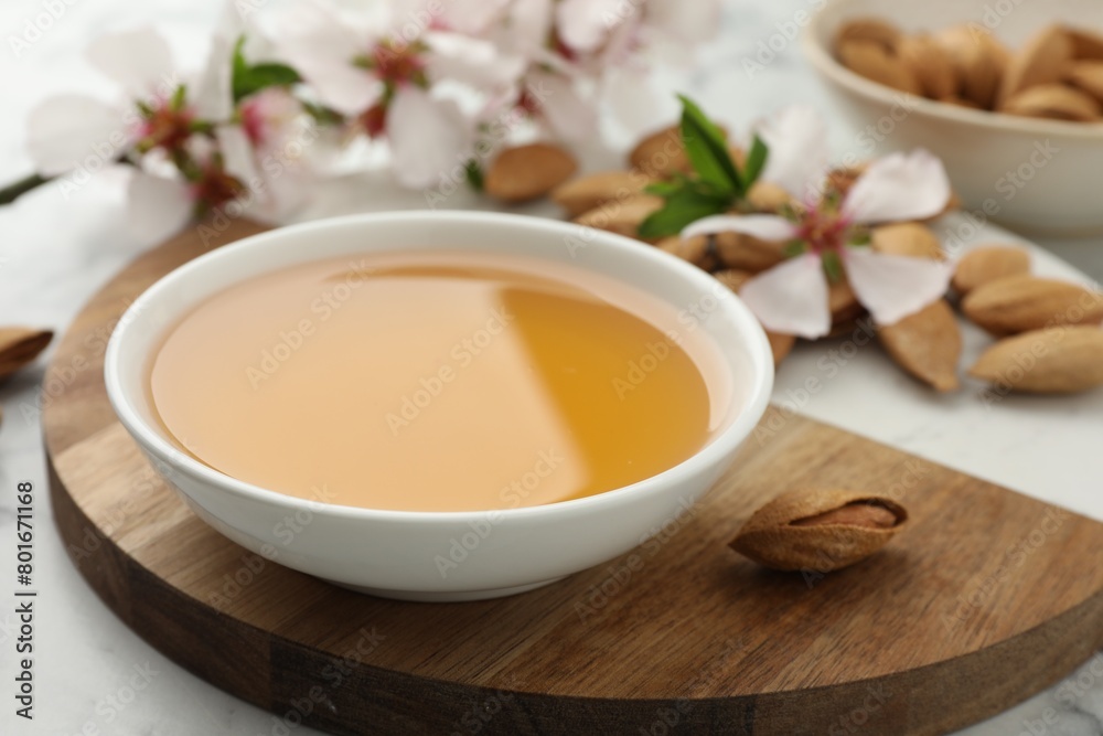 Almond oil in bowl, nuts and flowers on white table, closeup Almond oil in bowl, nuts and flowers on white table, closeup
