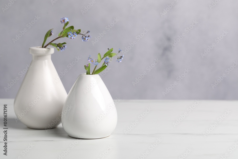 Beautiful forget-me-not flowers in vases on white marble table, closeup. Space for text Beautiful forget-me-not flowers in vases on white marble table, closeup. Space for text