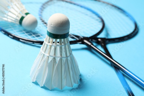 Feather badminton shuttlecocks and rackets on light blue background, closeup photo