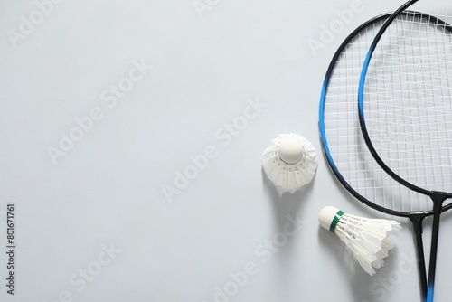 Feather badminton shuttlecocks and rackets on gray background, flat lay. Space for text photo