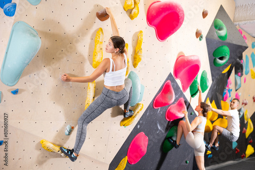 Motivated young girl climbing without ropes and harnesses on artificial bouldering wall in modern fitness center. Active lifestyle and recreation concept..