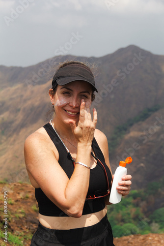 Latin female person applying sunscreen cream on her face for sun protection. Skin care concept. Hiking in the mountains. SPF.