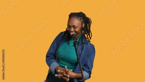 Cheerful motivational speaker talking in microphone doing stand up comedy, addressing audience, studio background. Funny woman using mic to tell hilarious joke and amuse spectators, camera A photo