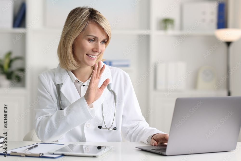 Smiling doctor with laptop having online consultation at table in office Smiling doctor with laptop having online consultation at table in office