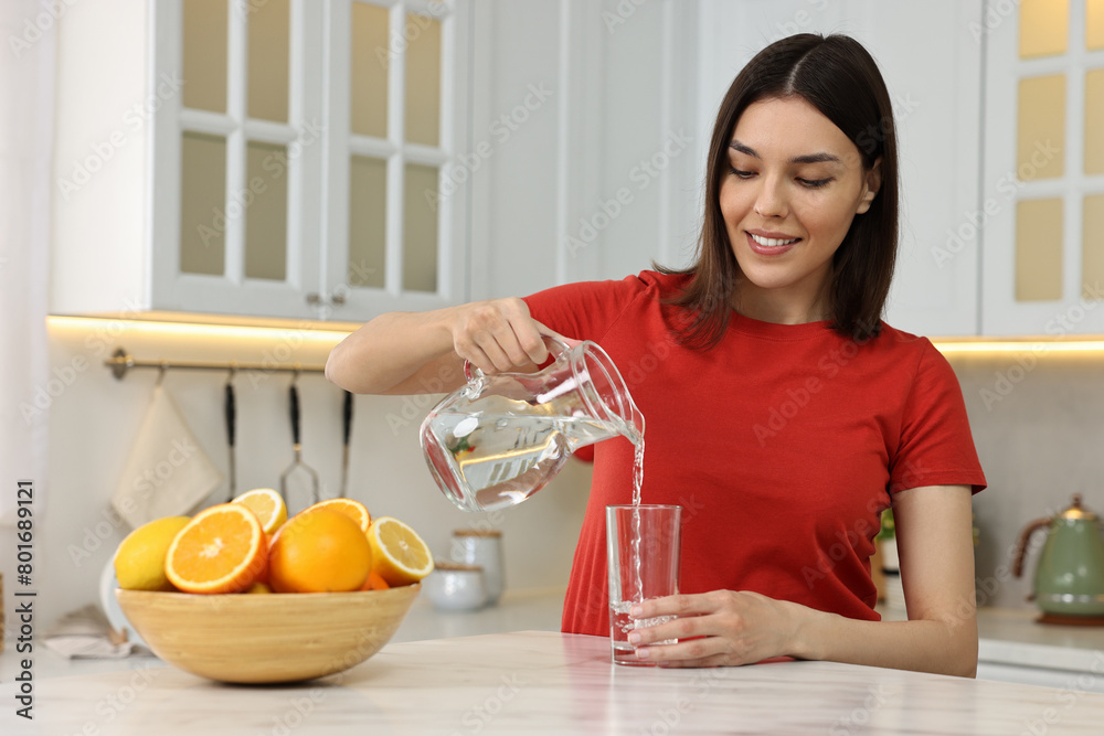Young woman pouring water into glass from jug in kitchen Young woman pouring water into glass from jug in kitchen