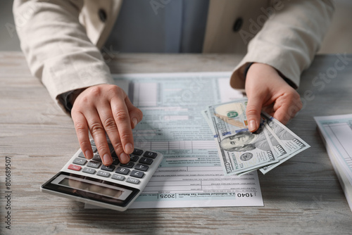 Payroll. Woman with dollar banknotes and calculator planning budget at wooden table, closeup
