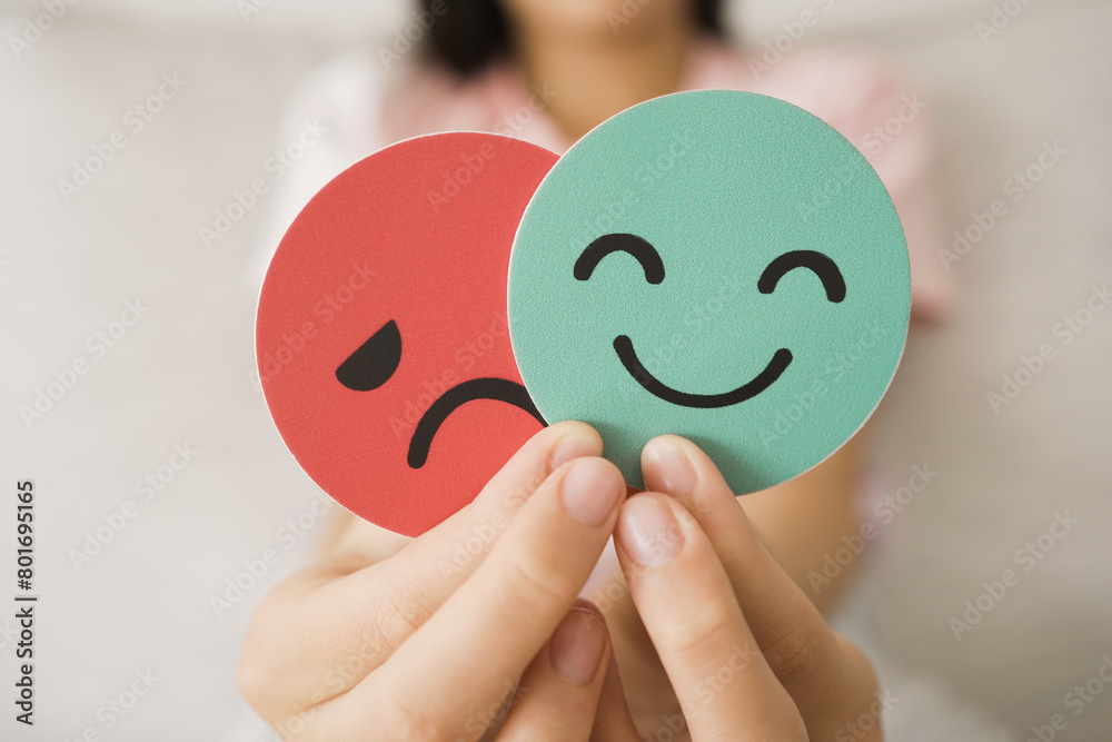 Preteen hands holding sad face hiding behind happy face, bipolar and depression, mental health, split personality, mood change concept Preteen hands holding sad face hiding behind happy face, bipolar and depression, mental health, split personality, mood change concept