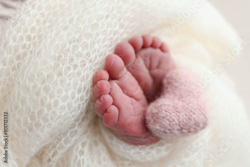 The tiny foot of a newborn baby. Soft feet of a new born in a white wool blanket. Close up of toes, heels and feet of a newborn. Knitted pink heart in the legs of a baby. Macro photography