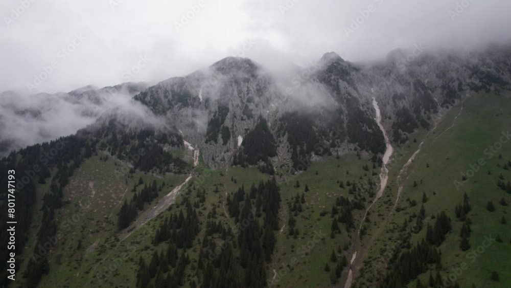 Misty mountain peaks with drifting clouds in a lush green valley, aerial view