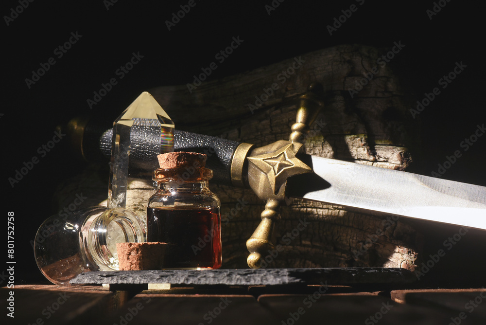 Magic potion bottle and sword on the old wooden table background front view. Witchcraft concept.