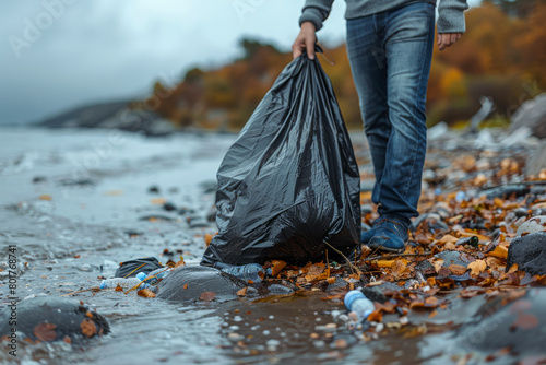 A person is holding a black plastic bag while walking on a beach