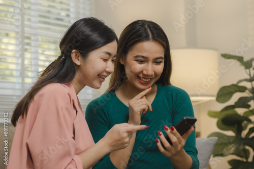 Two beautiful Asian women are using electronic devices to entertain themselves as a group activity in their apartment, Spend free time together on the sofa at home during the weekends.