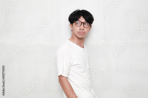 Young asian man wearing white t-shirt and glasses on white background looking to the side