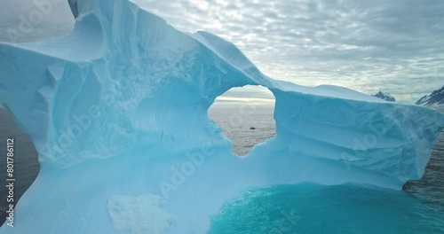 Giant blue melting iceberg with cave drifts ocean water. Drone fly inside ice glacier hole. Polar nature. Cold South Pole winter landscape. Wild nature people explore travel. Cinematic ecology scene.