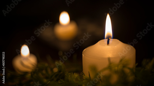 A large candle in focus and two candles in the background of the image. Three candles lit in the dark