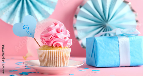 Delicious cupcake with question mark, gift box and decorations on pink background. Gender reveal party concept photo