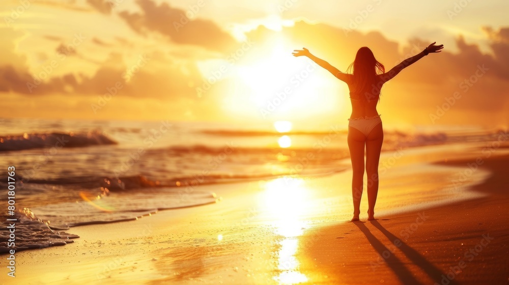 Silhouette of a woman with arms raised, enjoying the sunrise on a serene beach.