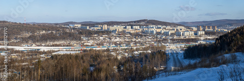 Tynda city, Amur region, Siberia, Russia. Winter panoramic city landscape. In the distance are residential buildings and hills. In the middle ground there is a railway. In the foreground is a road.