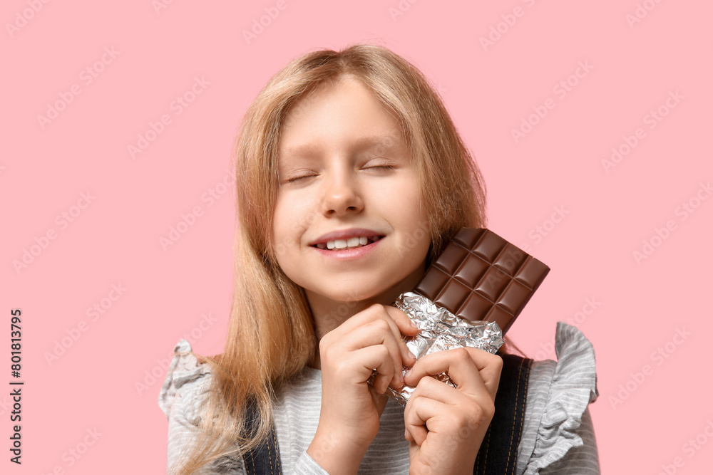 Cute little girl with sweet chocolate bar on pink background