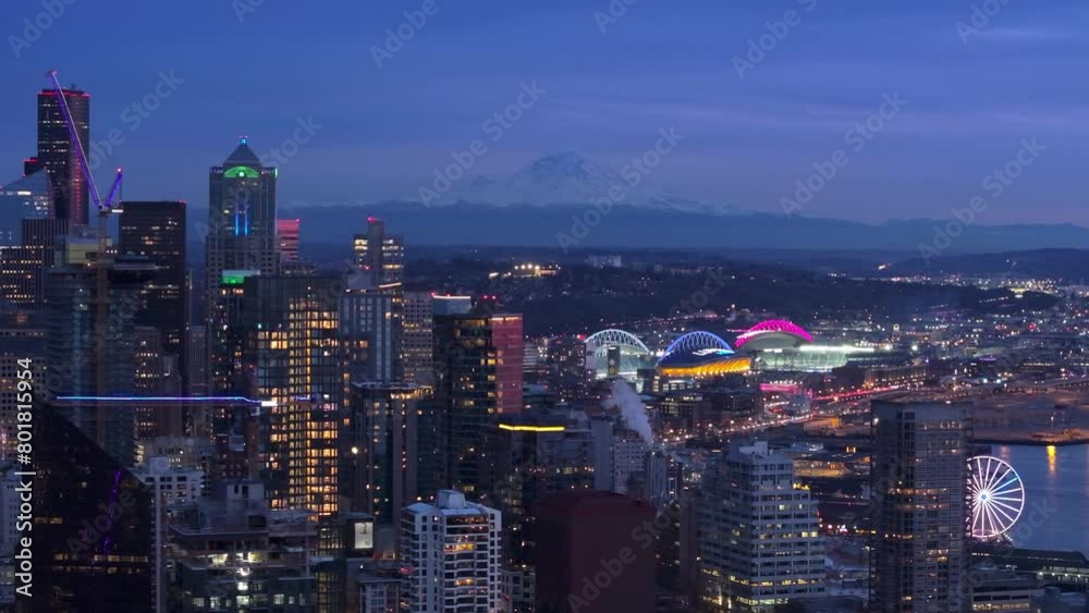 An aerial view captures the glowing cityscape of Seattle at dusk, showcasing Mount Rainier and the lit stadiums and Ferris wheel. A serene urban scene. 4K footage. An aerial view captures the glowing cityscape of Seattle at dusk, showcasing Mount Rainier and the lit stadiums and Ferris wheel. A serene urban scene. 4K footage.
