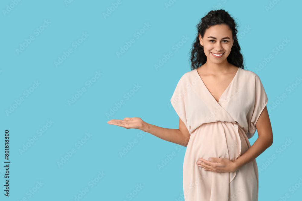 Beautiful young pregnant African-American woman pointing at something on blue background Beautiful young pregnant African-American woman pointing at something on blue background