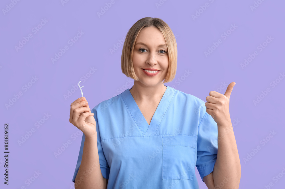 Female dentist with dental floss pick showing thumb-up on lilac background Female dentist with dental floss pick showing thumb-up on lilac background
