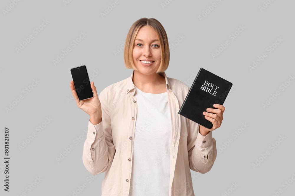 Happy adult woman with Holy Bible and mobile phone on white background Happy adult woman with Holy Bible and mobile phone on white background