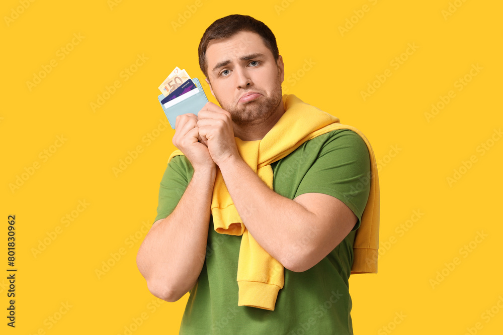 Young upset man holding wallet with credit cards on yellow background Young upset man holding wallet with credit cards on yellow background