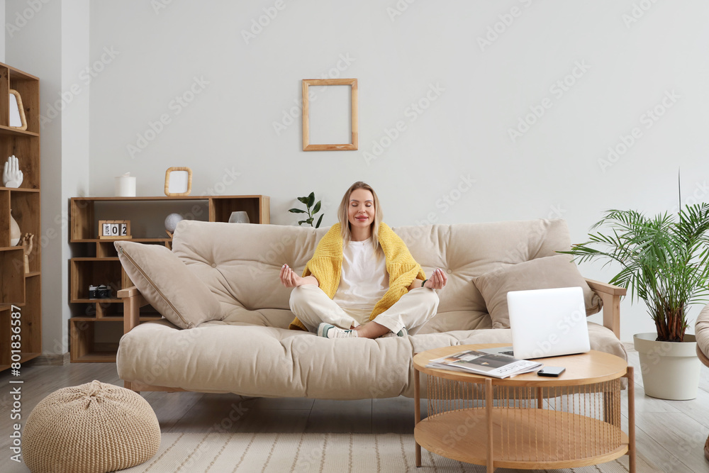Young woman meditating on sofa in stylish living room Young woman meditating on sofa in stylish living room