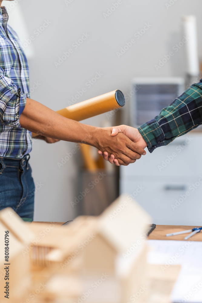 Young Asian forewoman and middle-aged foreman, achieving success through agreement and teamwork, symbolized by a handshake. Expertise in budgeting, design, and architectural planning.