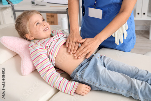 Female pediatrician examining little girl's belly on couch in clinic, closeup