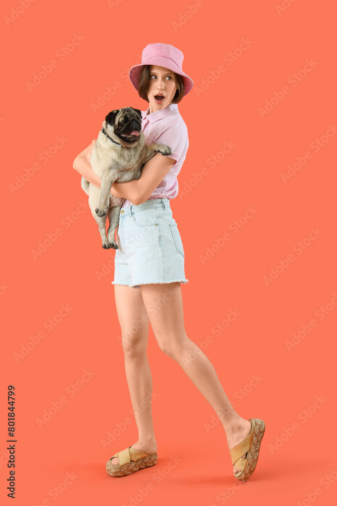 Fototapeta premium Surprised young woman with cute pug dog on orange background