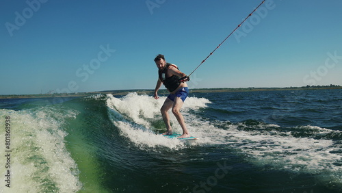 A man rides a wakeboard after a boat. Fun on the water during the hot summer on the lake. © Volodymyr