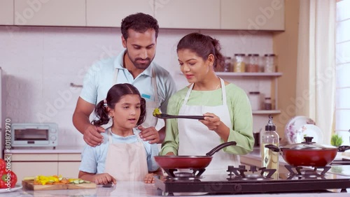 Happy daughter and father checking the food taste after cooking with mother at kitchen - concept of family bonding, leisure activities and weekend fun